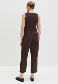 Braune Wildlederhosen mit entspannter Passform, ausgestattet mit Gesäßtaschen und einer glatten Textur, kombiniert mit einem eng anliegenden braunen Tank-Top.