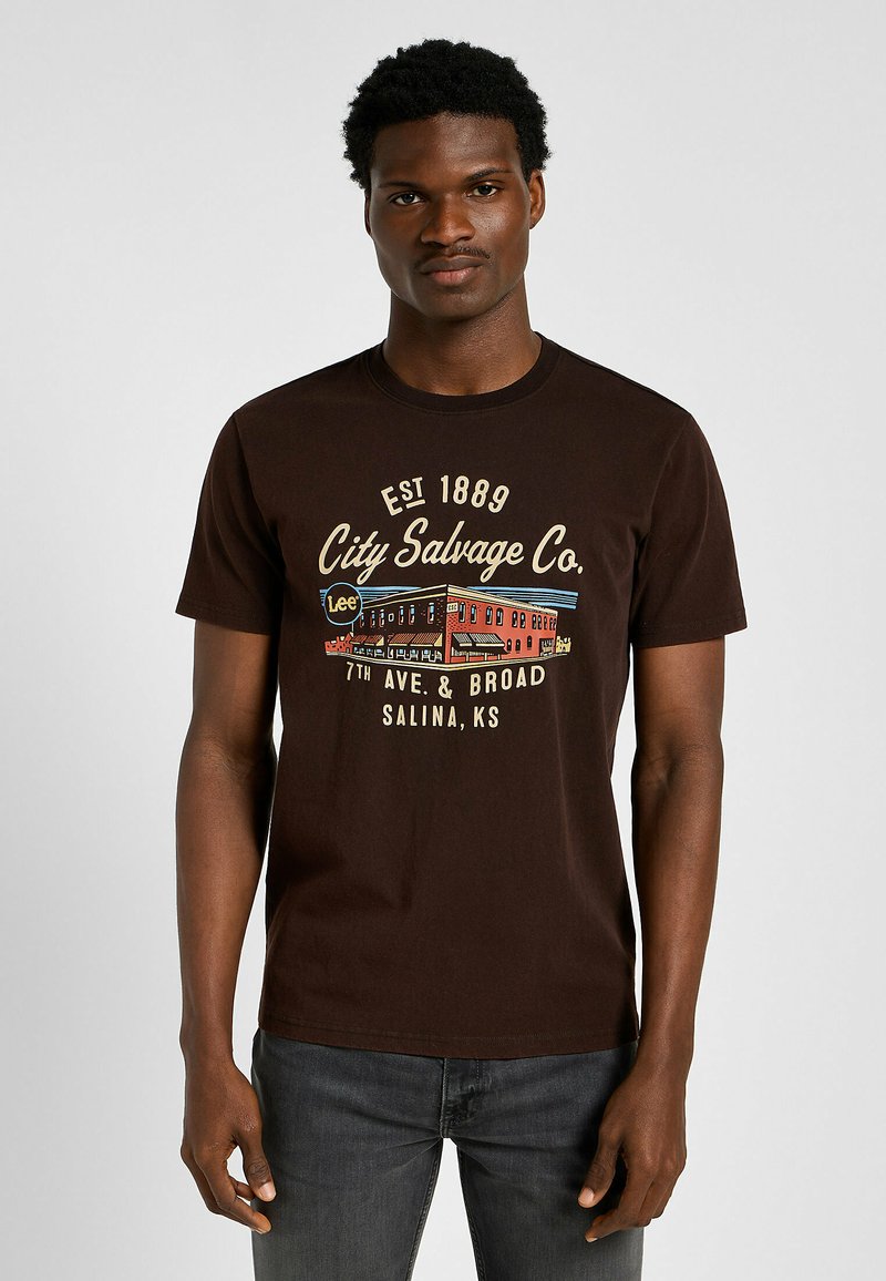 Camiseta de algodón marrón con un colorido estampado gráfico que incluye el texto "City Salvage Co." y una ilustración de un edificio vintage. Mangas cortas.