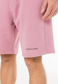 Lyserøde bomuldsshorts med en glat tekstur, som har en sidelomme og "PEGADOR" logo i en mørkere nuance på venstre søm.