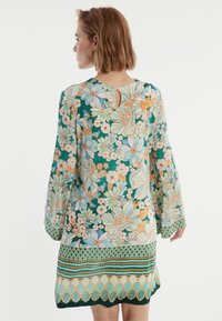 Robe fleurie à manches longues, avec un fond vert, des fleurs bleu clair et pêche, et un ourlet orné de motifs avec un col en trou de serrure.