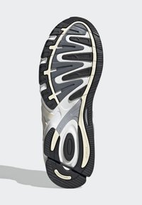 Atlétikai cipőtalp fekete gumiból és szürke díszítéssel, hullámos mintázattal, kiemelkedő tapadófelületekkel és látható márkajelzésekkel.