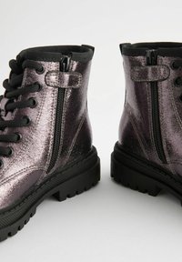Stivali alla caviglia metallici viola con lacci neri e cerniere, caratterizzati da una finitura testurizzata e una suola nera robusta.