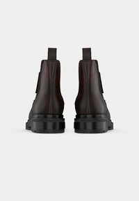 Botas de cano curto em couro castanho com um acabamento liso, apresentando uma sola preta robusta e um salto texturizado, projetadas para durabilidade e suporte.