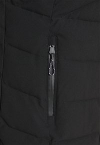 Giubbotto piumino nero con un design a quadrati inclinati, dotato di una tasca con zip e un laccio nero per un facile accesso.