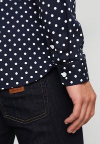 Marineblauwe shirt met witte stippen, voorzien van een knoopmanchet en een soepele stof. Draag het met donkere jeans met een logopatch.