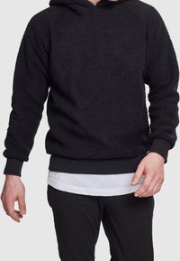 Czarna polarowa bluza z fakturowanym wykończeniem, z przednią kieszenią i ściągaczami na rękawach. Nosi się ją na białej, warstwowej koszuli.