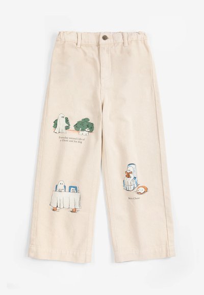 Pantalon beige avec des illustrations d’un fantôme et d’un chien dans différentes scènes, y compris assis, en train de lire et cachés derrière une table.