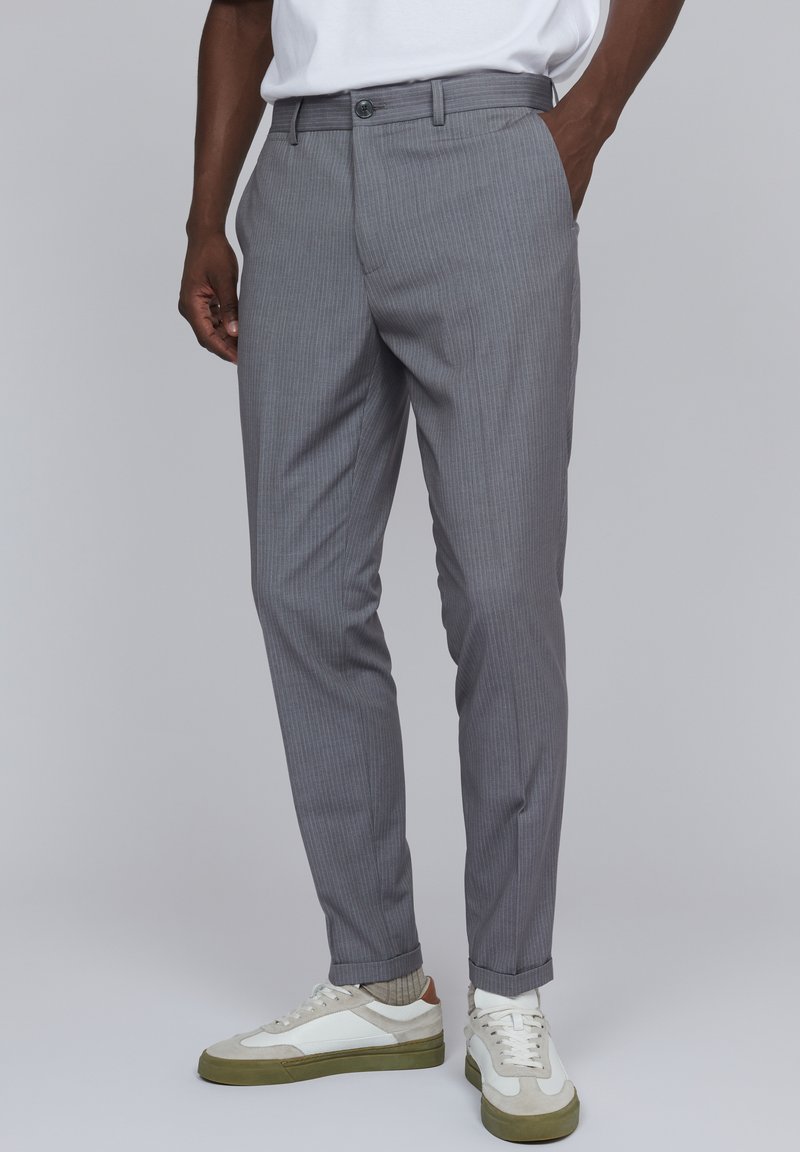Pantalones de rayas grises hechos de una tela ligera, con un ajuste slim, bolsillos frontales y cierre de botón, combinados con zapatillas blancas.