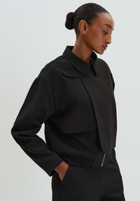 Zwarte cropped sweatshirt met een gestructureerde kraag, een voorflap en een ritsdetail aan de onderkant. Gemaakt van een soepele stof; heeft ruime mouwen.