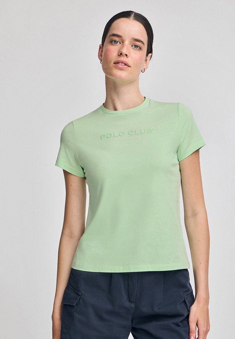 Camiseta de manga corta verde claro con cuello redondo, que presenta el texto 'POLO CLUB' en relieve. Tela suave, diseño ajustado, estilo sencillo.