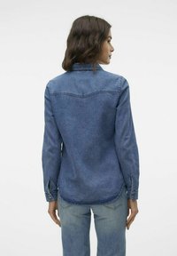 Denimhemd in Mittelblau, langärmlig mit Knopfmanschetten, Vorderpasse-Detail, abgerundetem Saum und entspanntem Schnitt. Glatte Textur, lässiges Design.