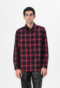 Camisa de cuadros de manga larga para hombre en patrón de cuadros rojos y negros, con cuello button-down y un sutil logo en el pecho.
