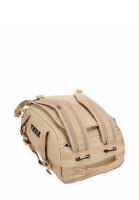 Sac à dos Thule en beige, doté de bretelles en maille rembourrées, de doubles poignées latérales, de fermetures éclair et d'une surface texturée pour la durabilité et le style.