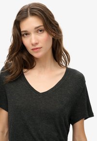 Sort v-hals t-shirt med en spraglet tekstur og guldpletter, korte ærmer og et subtilt logo på brystet.