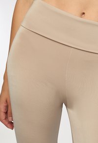Leggings beige elasticizzati con vita alta, texture liscia e una silhouette aderente che arriva a metà coscia. Dettagli delle cuciture minimi.