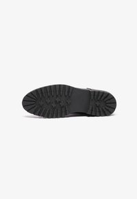 Sola di scarpa nera con scanalature profonde, realizzata in materiale gommoso e di forma arrotondata. I motivi a croce evidenti migliorano la presa e la durata.