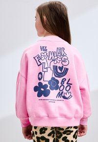 Lyserød sweatshirt med et grafisk design af blomster og tekst på ryggen. Blødt stof, afslappet pasform, ribstrikkede manchetter og kant.