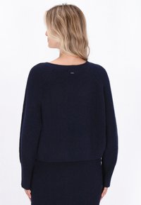 Granatowy sweter z prążkowanej dzianiny z krótkim krojem, teksturowanym materiałem i okrągłym dekoltem. Subtelne logo na plecach przy dekolcie.