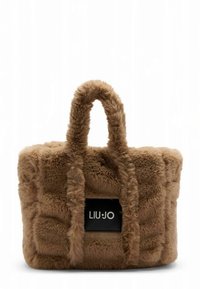 Sac à main en fausse fourrure beige avec un design texturé et matelassé. Dispose de longues anses douces et d'un patch noir avec logo à l'avant.
