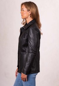 Black leather jacket with a structured design, front zipper, and adjustable cord, paired with blue jeans for a casual look.