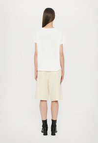 Bílá bavlněná trička s kulatým výstřihem a krátkými rukávy, doplněná béžovými šortkami. Černé kotníkové boty dokončují outfit.