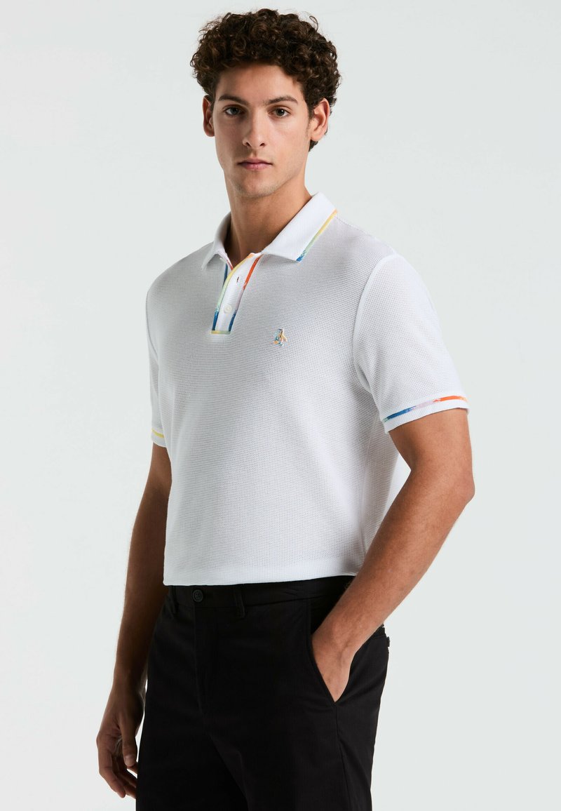 Witte polo shirt met een gestructureerde stof, voorzien van een kleurrijke gestreepte kraag en mouwen. Geborduurd logo op de borst. Zwarte broek.