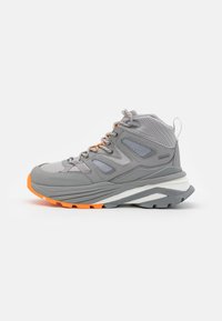Chaussure de randonnée mi-haute étanche grise avec des accents orange, des panneaux texturés et des détails réfléchissants. Semelle en couches blanche et grise pour un soutien optimal.