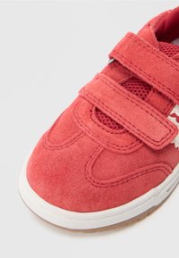 Red suede shoe with a rounded toe, featuring two Velcro straps, mesh accents, and a white rubber sole with a textured bottom.