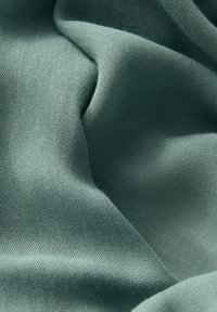 Tissu tissé vert pâle doux avec une texture fine et de légères plis et rides.