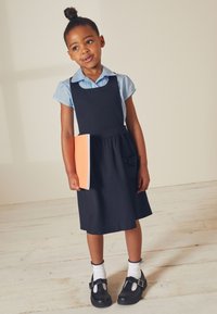 Marinblå klänning med en åtsittande överdel och plisserad kjol, ihop med en ljusblå skjorta med krage. Svarta skor och vita strumpor fulländar outfiten.