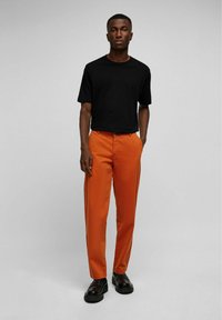 Zwarte katoenen t-shirt, oranje broek en zwarte instappers. De broek heeft een recht model. Eenvoudig ontwerp zonder zichtbare patronen.