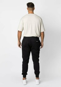 Zwarte joggerbroek met een achterzak en elastische boorden, gecombineerd met een losse, korte mouwen beige t-shirt. Witte sneakers maken de look af.