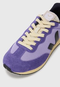 Purple sneakers with suede and mesh materials, featuring cream laces, black logo accents, and a contrasting beige midsole.
