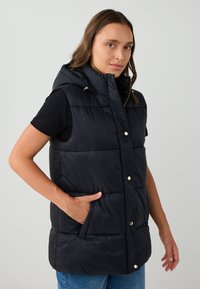 Gilet imbottito nero con colletto alto, design senza maniche, tasche frontali e bottoni a pressione metallici, con una texture liscia e lucida.