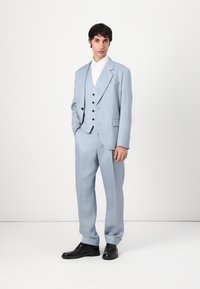 Traje azul claro de tela suave, con chaqueta de un solo botón, chaleco a juego con botones y pantalones a medida. Zapatos negros.