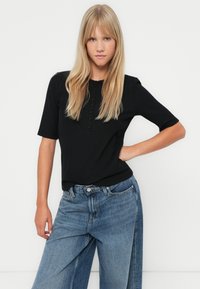 Svart stripete kortermet topp med knappestolpe, kombinert med vide blå denimjeans med høy midje og avslappet passform.