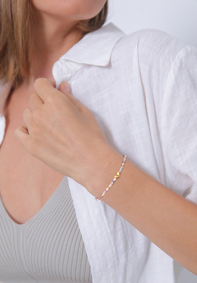 Armband med gulddetaljer som har flerfärgade pärlor i pastellfärger, designad för att passa bekvämt på handleden, med varierande texturer och former.