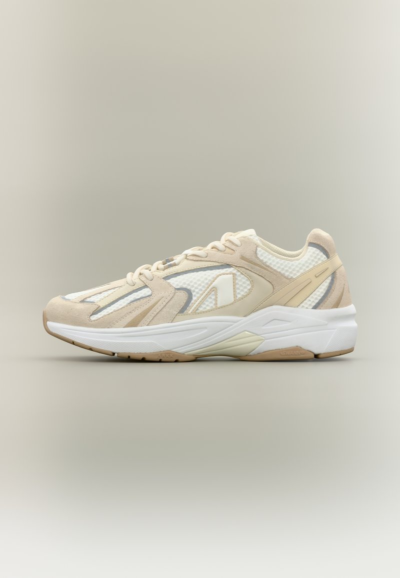 Smėlio spalvos sportinė avalynė su tinkleliu ir zomšos viršumi, stora balta pado dalimi, aerodinamišku dizainu ir subtiliais pilkais akcentais.