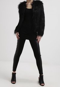Chaqueta negra de piel sintética con mangas largas, combinada con un vestido negro ajustado y leggings negros de cintura alta. Botines decoran el look.