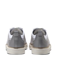 Zapatillas grises y blancas con un upper texturizado, detalles en cuero liso, un diseño en forma de ondas y una suela a rayas color crema.