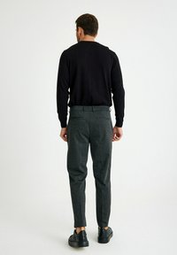 Zwarte lange mouwen trui gecombineerd met donkergrijze gestreepte broek. De outfit heeft een aansluitende pasvorm en wordt aangevuld met zwarte sneakers.