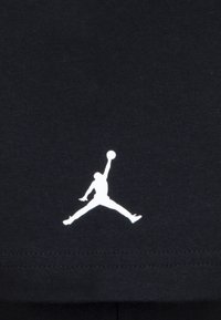 Svart tyg med en vit Jumpman-logo. Designen visar en figur med utsträckta lemmar som håller en basketboll, centralt placerad.