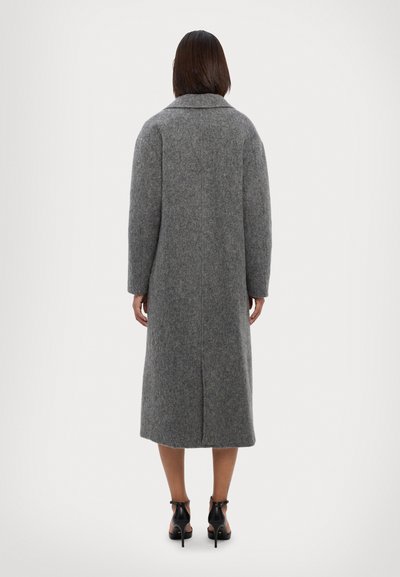 Grauer Wollmantel mit langem Schnitt, breitem Kragen und langen Ärmeln. Verfügt über eine Mittelnaht hinten und einen Schlitz am Saum. Schwarze Schuhe mit Knöchelriemen.