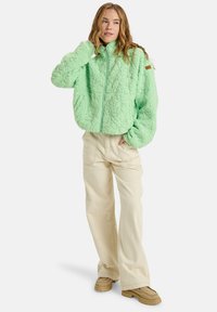 Mint green, textured fleece jacket with a high collar and front zipper, paired with cream wide-leg pants and tan shoes.