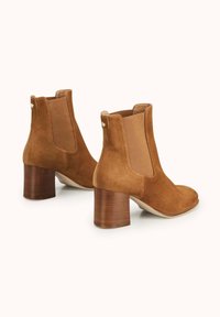 Bottines en daim marron avec des panneaux latéraux élastiques, un bout arrondi et un talon bloc en bois texturé, avec un petit détail d'onglet à l'arrière.