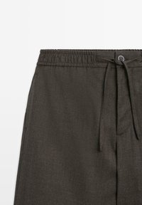 Pantaloni a scacchi grigio scuro con vita elasticizzata, cordoncino e chiusura con bottone, texture strutturata e tasche.