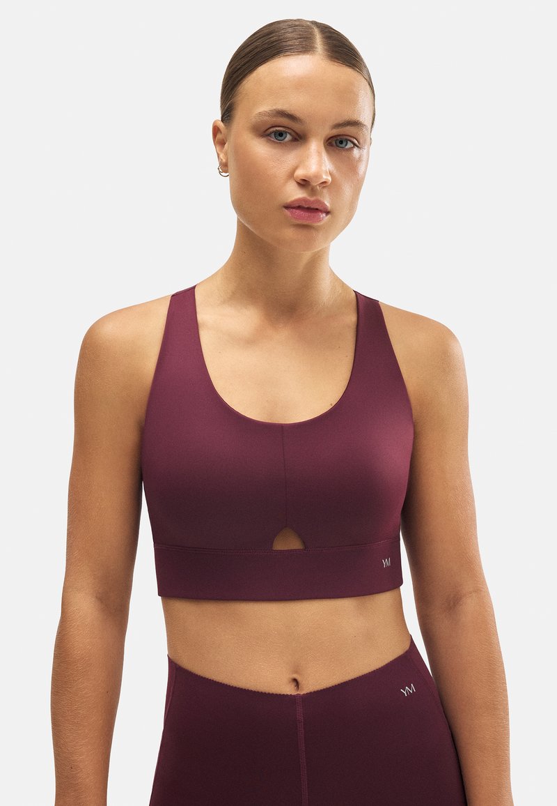 Sujeción deportiva burdeos con escote redondeado, detalle en forma de llave y tirantes anchos. Fabricado con una tela suave y elástica para mayor comodidad y soporte.