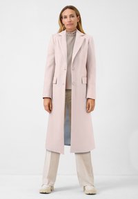 Ljusrosa lång kappa i ullblandning med notad krage, tv�å framfickor och en knappslutning. Stylad över en plisserad topp och byxor.