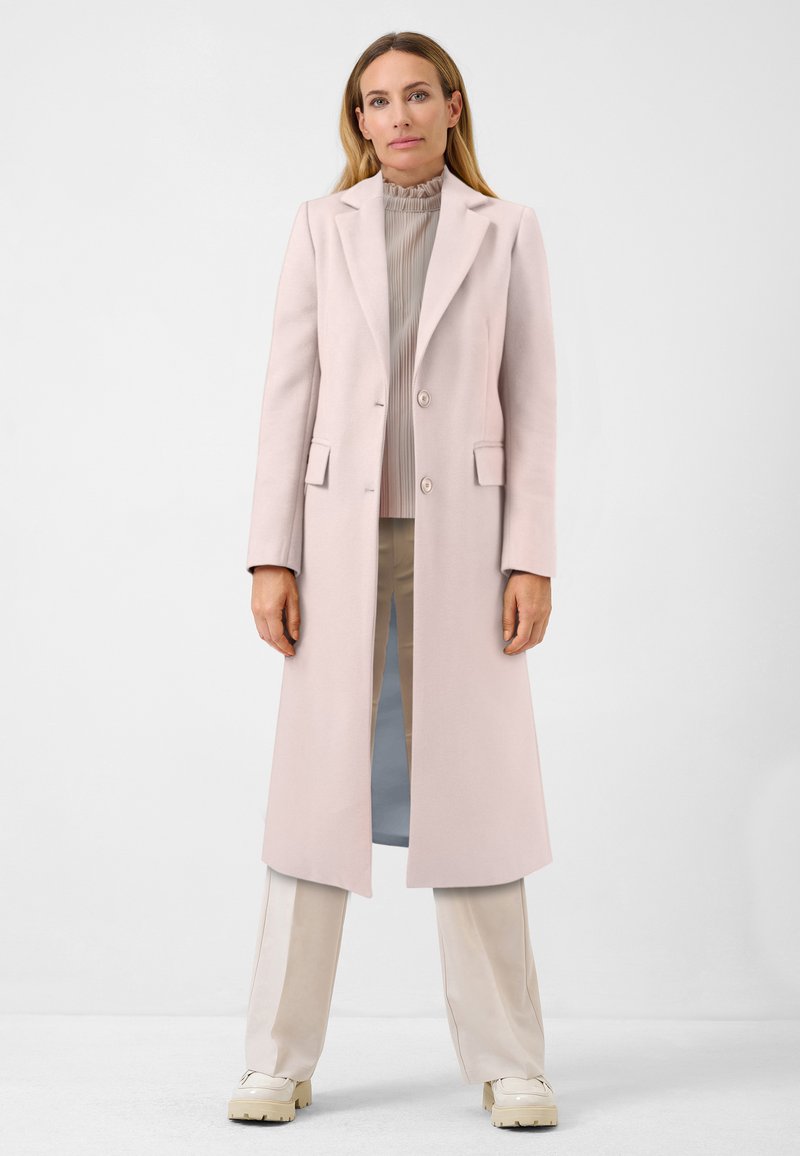 Ljusrosa lång kappa i ullblandning med notad krage, två framfickor och en knappslutning. Stylad över en plisserad topp och byxor.