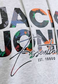 Grijze hoodie met grote zwarte tekst en kleurrijke verfspat accenten. Inclusief trekkoorden en een merklogo ontwerp.